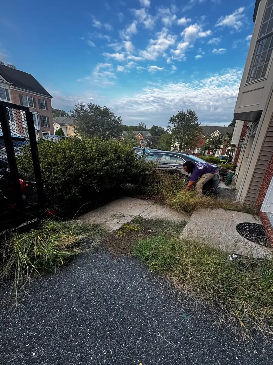 A Sisters With A Mower crew member clearing overgrown weeds out of the front bed